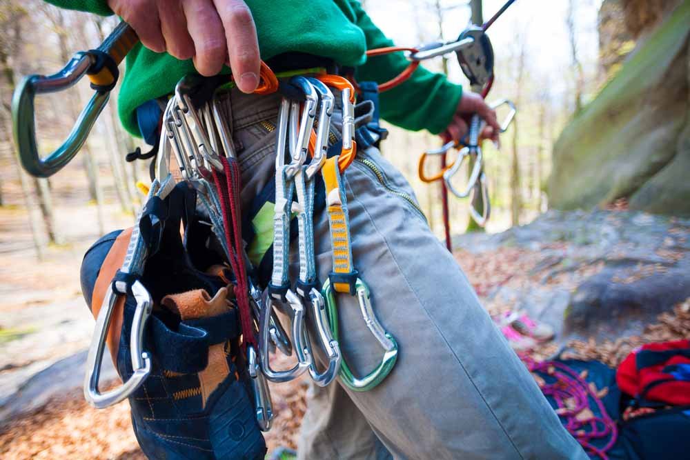 hand placing quickdraws on harness for lead climbing