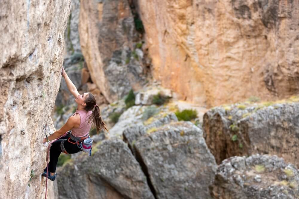 young woman lead climbing on arete