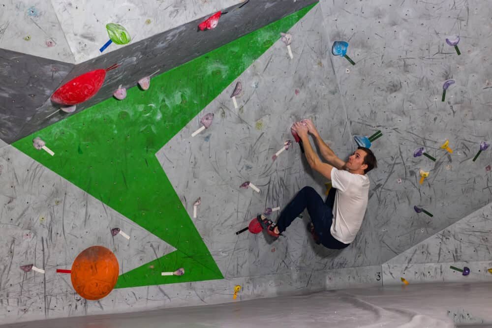 man crouching on bouldering wall inside preparing to dyno